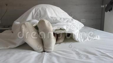 脚钻进了床上.. 男人和女人的脚从温暖的冬毯下伸出来。